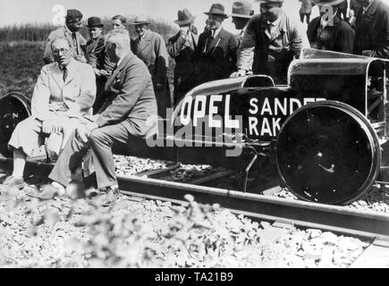 Fritz von Opel (l.) assis devant la voiture fusée construite par lui et l'ingénieur Sander. Le véhicule atteint une vitesse de 100 km / h en quelques secondes. Banque D'Images