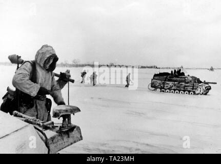 Un Allemand Jagdpanzer IV (réservoir de chasse), de concert avec les fantassins, des avances sur les champs de neige de la Puszta hongroise. L'un des hommes de gauche est porteur d'une coupure le Panzerfaust.véhicule est un véhicule de transport de troupes et. Kfz.251. Visiblement, le frein de bouche du Jagdpanzer est manquant. Ils sont souvent démantelés, comme ils excitèrent trop de poussière, et de cette façon ils ont révélé leur propre position. Banque D'Images