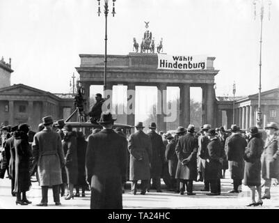 Une banderole est accrochée sur la porte de Brandebourg à l'appel 'Voter pour Hindenburg'. Certaines personnes sont debout devant la porte de Brandebourg, et observent la bannière. Un caméraman est également présent. Banque D'Images