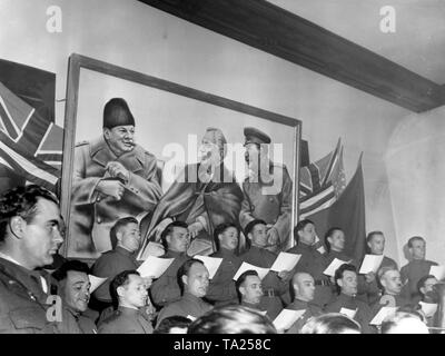 Un des soldats russes' choir chante à l'administration centrale soviétique à l'occasion de la rencontre avec les troupes américaines. Dans l'arrière-plan une photo montrant les chefs d'état des nations alliées (de gauche à droite : Churchill, Roosevelt, Staline) lors de la conférence de Yalta. Banque D'Images