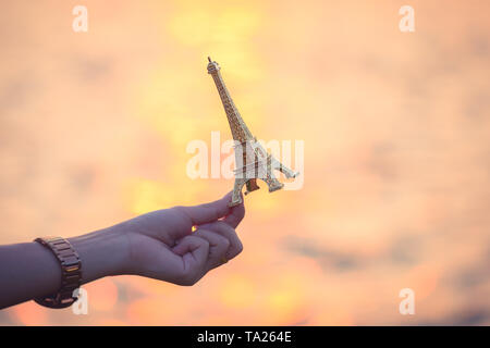 Main tenant une figurine de la tour Eiffel au coucher du soleil . la culture française . Banque D'Images