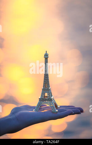 Main tenant une figurine de la tour Eiffel au coucher du soleil . la culture française . Banque D'Images