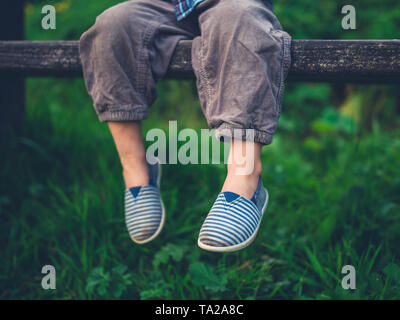 Les pieds d'un petit enfant assis sur un banc dans la nature Banque D'Images