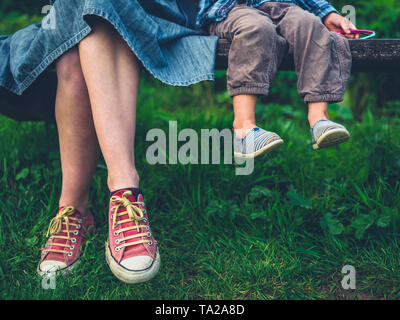 Les jambes d'une jeune mère et son enfant se détendre sur un banc dans la nature Banque D'Images