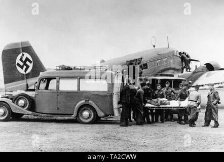 Photo d'un soldat blessé de la légion Condor, est transporté par des camarades sur une civière de l'ambulance voiture pour une ambulance aérienne (Junkers Ju 72) de l'allemand Lufthansa. Une grande croix gammée est affiché sur l'empennage vertical. Banque D'Images