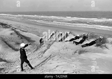 Au cours d'un combat de formation des recrues ont trouvé refuge avec leurs fusils sur une dune alors que l'instructeur donne des instructions. Banque D'Images