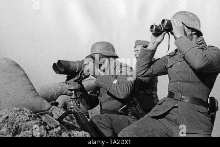 Photo non datée d'un poste de commandement à l'avant dans la guerre civile espagnole. Derrière une barrière de sable, un caporal (sur la gauche debout à un Scheinwerferichtweiser 35) et un autre soldat (avec des jumelles) regardent la bataille. Banque D'Images