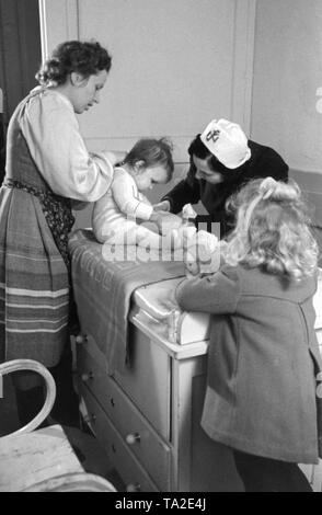 Les infirmières de la NS-Volkswohlfahrt prendre soin d'un enfant dans un service de la "Hilfswerk Mutter und Genre'. À droite, une fille avec une poupée. Photo non datée. Banque D'Images