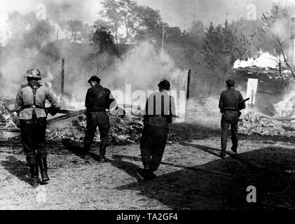 Les soldats allemands recherchez un village en feu avec des armes tirées sur le front de l'Est (sans doute l'Est de la Pologne). Les maisons qui étaient pour la plupart construit de bois a pris feu par de lourdes d'artillerie soviétique. Photo de l'entreprise de propagande (PK) : correspondant de guerre Koenneke. Banque D'Images