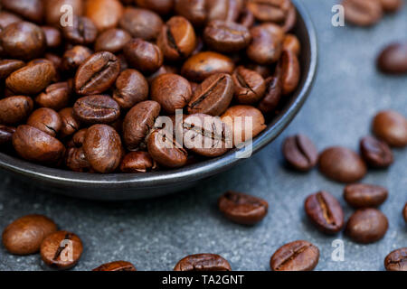 Grains de café dans un bol noir sur fond gris ardoise. Close up. Banque D'Images