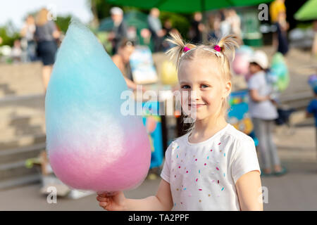 Jolie petite blonde caucasienne kid girl holding dans la main stick avec un gros coton multicolore candy sweet au parc de la ville pendant l'été ou juste carnival Banque D'Images