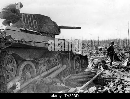 Un soldat allemand grimpe un abattu T-34 sur le Front Volkhov. À côté, un soldat tué sur le sol. Les combats ont détruit de vastes zones de la forêt. Photo de l'entreprise de propagande (PK) : correspondant de guerre Schuerer. Banque D'Images