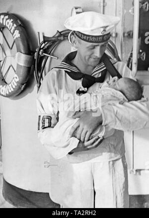 Photo d'un marin tenant un bébé dans ses bras sur le pont du croiseur lourd « Deutschland gisant dans les rues de Valence en Espagne durant la guerre civile en août 1936. La France a apporté à des réfugiés allemands Gérone, où elles ont été prises en charge par le vapeur de l'organisation Nazie Kraft durch Freude ('force par la joie") Monte Sarmiento (lancé en 1924, Monte-Klasse, coulé en 1942). Banque D'Images