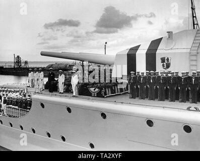 Photo du pont supérieur du croiseur lourd « Deutschland avec les cercueils de ses membres d'équipage, qui ont été tués dans le bombardement d'avions républicains pendant la Guerre Civile Espagnole près de Ibiza en juin 1937, dans le port de Wilhelmshaven sur la mer du Nord. À côté des cercueils ornés de l'étoile de la marine et des couronnes de fleurs, la garnison s'alignent en uniforme. Derrière, il y a la tourelle avec trois canons (calibre de 28cm). Dans l'arrière-plan, l'installations portuaires. Banque D'Images