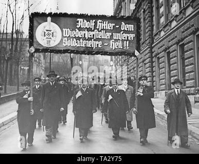 Au cours de l'allemand des Sudètes, membres de la guerre nationale-socialiste des soins de la victime (NSKOV) mars à Reichenberg (aujourd'hui Liberec). Dans le plébiscite, les votes sont exprimés sur l'annexion des Sudètes au Reich allemand. Sur l'affiche : "Adolf Hitler - le restaurateur de notre honneur de soldat- Heil ! !'. Banque D'Images