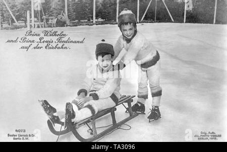 Prince héréditaire Wilhelm (gauche) assis avec son jeune frère le prince Louis Ferdinand (droit debout) sur une patinoire. Les deux princes porter des patins à glace. Le Prince Wilhelm est assis sur un traîneau en bois, Prince Louis Ferdinand repose sur les épaules de son frère. Banque D'Images