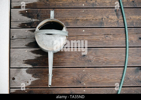 Arrosoir en métal rétro vu de dessus debout sur une terrasse en bois humide hachée avec un tuyau de jardin Banque D'Images