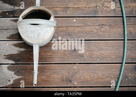 Arrosoir en métal rétro vu de dessus debout sur une terrasse en bois humide hachée avec un tuyau de jardin Banque D'Images