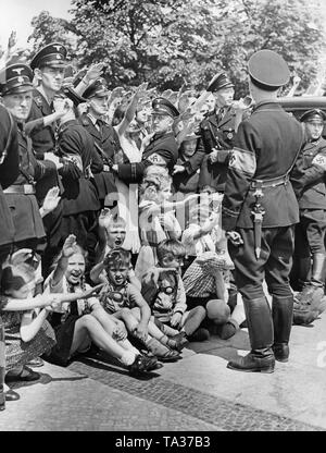 Photo d'un groupe de spectateurs enthousiastes sur l'Unter den Linden Strasse à Berlin, qui donnent le salut à Hitler la marche des soldats de la légion Condor à l'occasion de leur retour d'Espagne le 6 juin 1939. Ils sont retenus par des SS. Les enfants sont assis sur la chaussée. Banque D'Images