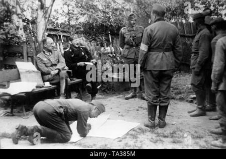 Les prisonniers russes sont interrogés par des officiers de la Wehrmacht sur le front de l'est près de Panjewitsch. Assis sur le banc, un officier et un agent de la Panzertruppe, sur la gauche des soldats de l'Armée Rouge. Photo : reporter de guerre Tannenberg. Banque D'Images