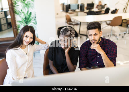 Groupe d'étudiants de l'université internationale s'amusant à étudier en bibliothèque, trois collègues de travail moderne de l'espace de co-working et parler tout en souriant Banque D'Images