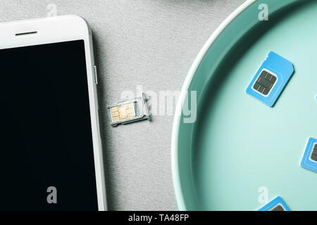 Plaque avec cartes SIM et téléphone mobile sur fond gris Banque D'Images