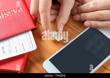 L'insertion de la femme dans la carte sim de téléphone mobile sur table en bois, gros plan Banque D'Images