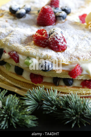 Gros plan du mille-feuilles de Noël dessert à la crème et petits fruits, décoration sapin fond sombre Banque D'Images