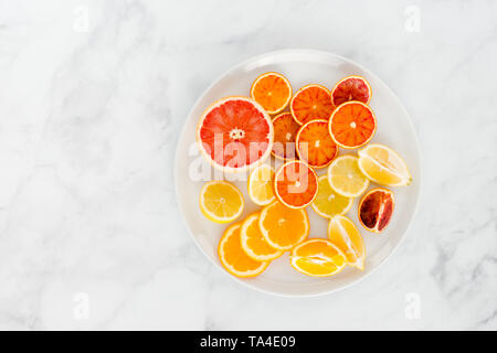 Couper les oranges, orange sanguine, citron et pamplemousse sur une grande assiette blanche et blanc en arrière-plan avec beaucoup d'espace de copie. Vue d'en haut. Banque D'Images