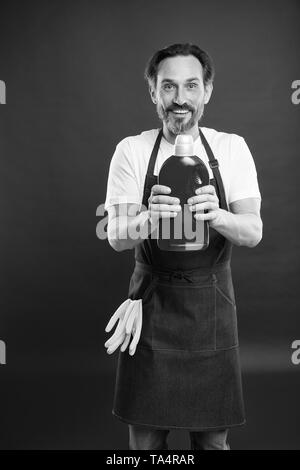 Service de nettoyage et de service à la personne. L'homme à tenir avec des gants tablier bouteille plastique savon liquide de nettoyage chimique. Journée de nettoyage d'aujourd'hui. Accueil nettoyage barbu. La garde de la propreté et l'ordre. Banque D'Images