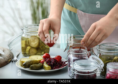 Woman putting de savoureux légumes fermentés sur la plaque dans la cuisine Banque D'Images