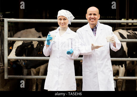 Portrait de deux vétérinaires souriant vêtu de blanc et d'un verre de lait frais en étable Banque D'Images