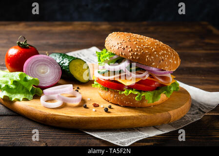 Burger sandwich au jambon, fromage et légumes sur une planche en bois avec des ingrédients. Copy space Banque D'Images