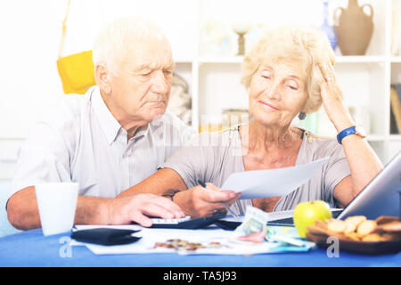 Couple frustrés face à des ennuis financiers table avec titres, espèces et calculatrice Banque D'Images