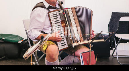 Un accordéoniste en vêtements traditionnels bavarois joue de l'accordéon sur la scène. L'accordéoniste joue l'instrument de musique. Banque D'Images