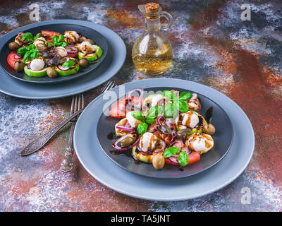 Deux bols de délicieuse salade, légumes grillés, mozzarella, olives, basilic et sauce balsamique sur fond rouille. Cuisine méditerranéenne Banque D'Images