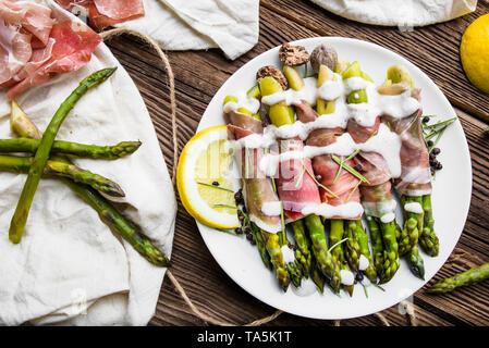 Les asperges vertes fraîches cuites avec du jambon et de la sauce sur le plat, vue du dessus Banque D'Images