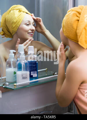 Portrait of smiling woman wearing towel après la douche à la recherche d'elle-même dans le miroir Banque D'Images