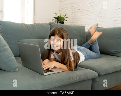 Beau charmant mignon lycéenne jouer et surfer sur l'Internet sur ordinateur portable en souriant et en étant couché sur le canapé à la maison. La technologie numérique, interne Banque D'Images