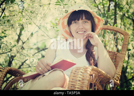 Fille de détente en fauteuil contre bloom garden Banque D'Images