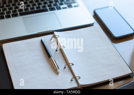 L'espace de travail, vue du dessus. Ordinateur portable, téléphone mobile et ordinateur portable ouvert avec un crayon beige sur bureau. Feuilles de bloc-notes sur les supports d'argent stylo à bille automatique, Banque D'Images