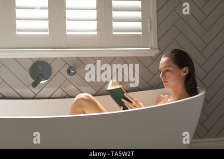 Belle femme lisant un livre dans la baignoire Banque D'Images