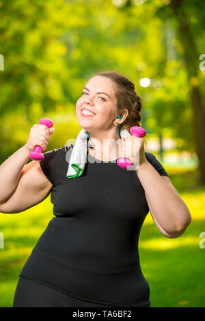 Portrait de femme verticale surdimensionnée avec haltères en main est engagé dans le sport dans le parc Banque D'Images