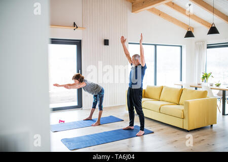 Un couple à l'intérieur à la maison, faire de l'exercice dans la salle de séjour. Banque D'Images