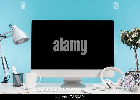 Lieu de travail avec ordinateur, lampe, papeterie et casque sur tableau blanc sur fond bleu Banque D'Images