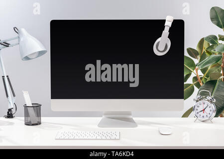 Lieu de Travail avec casque sur l'écran d'ordinateur, lampe et papeterie sur table blanc sur fond gris Banque D'Images