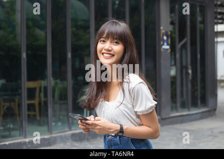 Happy asian woman holding smart phone in front of restaurant Banque D'Images