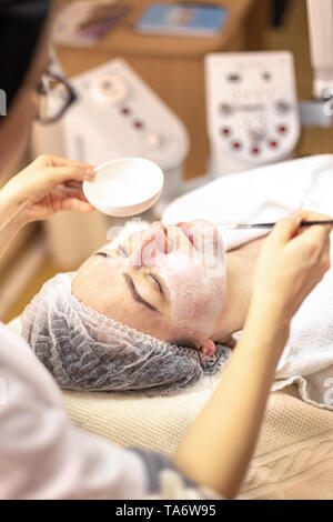 L'application Cosmetologist masque sur du visage dans le spa beauté. Woman getting facial care par boucher à spa salon Banque D'Images