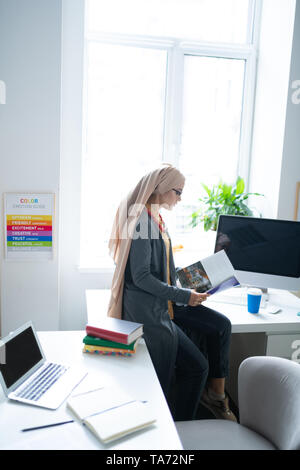 Enseignant portant hijab assis près de la fenêtre et reading book Banque D'Images