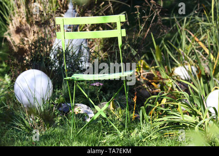 Close up of lonely vert isolé chaise pliante en bois dans le jardin de graminées, de roseaux vert électrique, lampes rondes, près de statue en pierre bouddha floue Banque D'Images